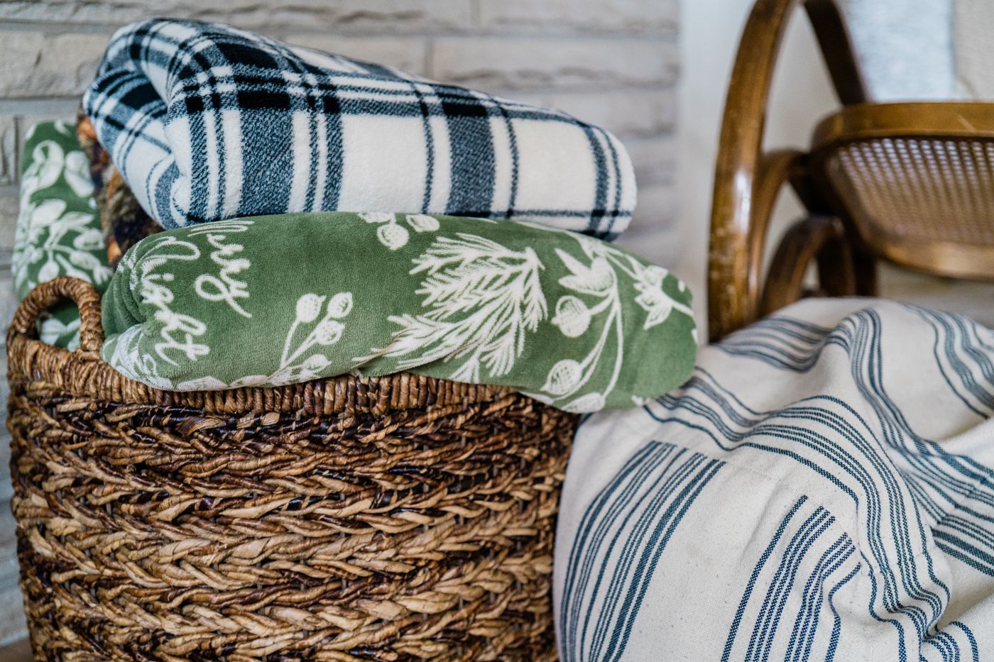 Folded throws stored in a woven basket beside a chair.