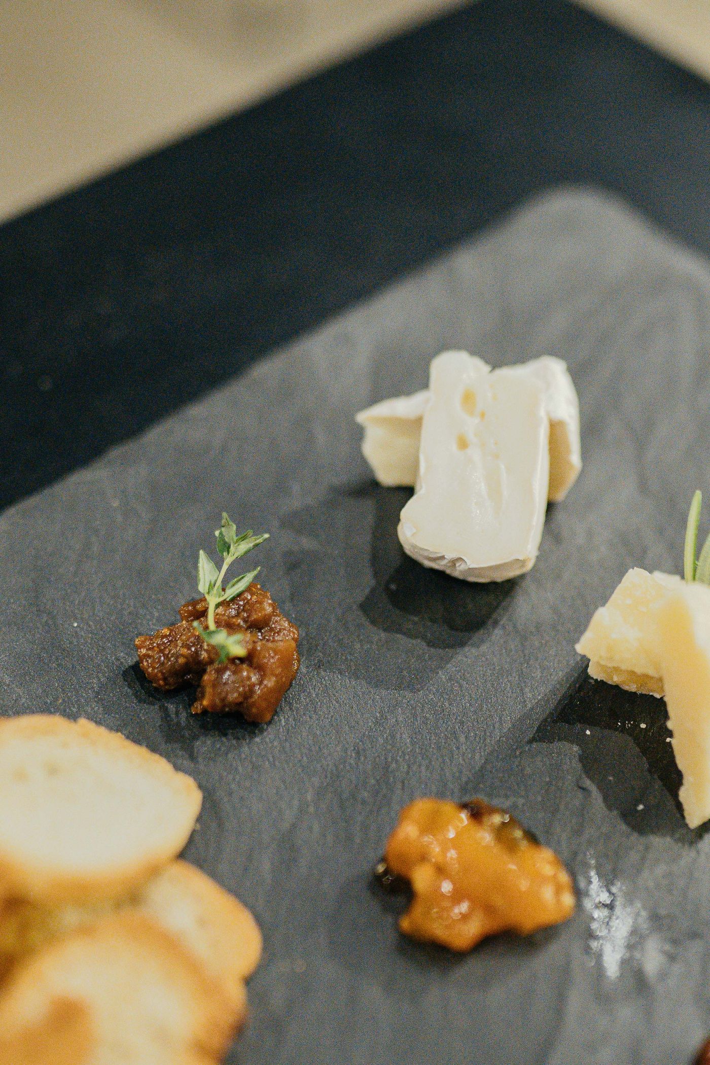 Several cheeses and chutney arranged with space on a dark serving board.