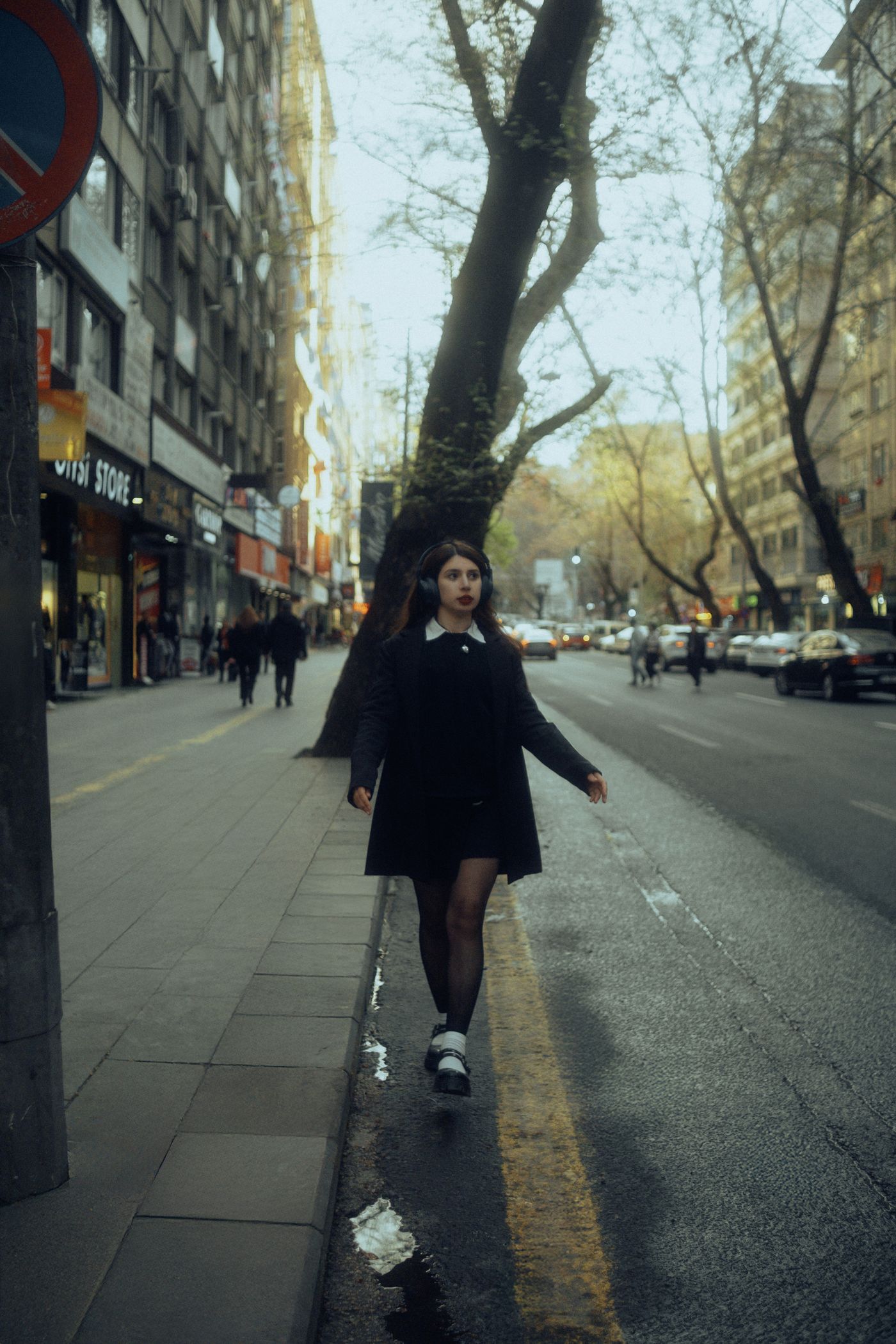 A woman walking along a tree-lined city street.