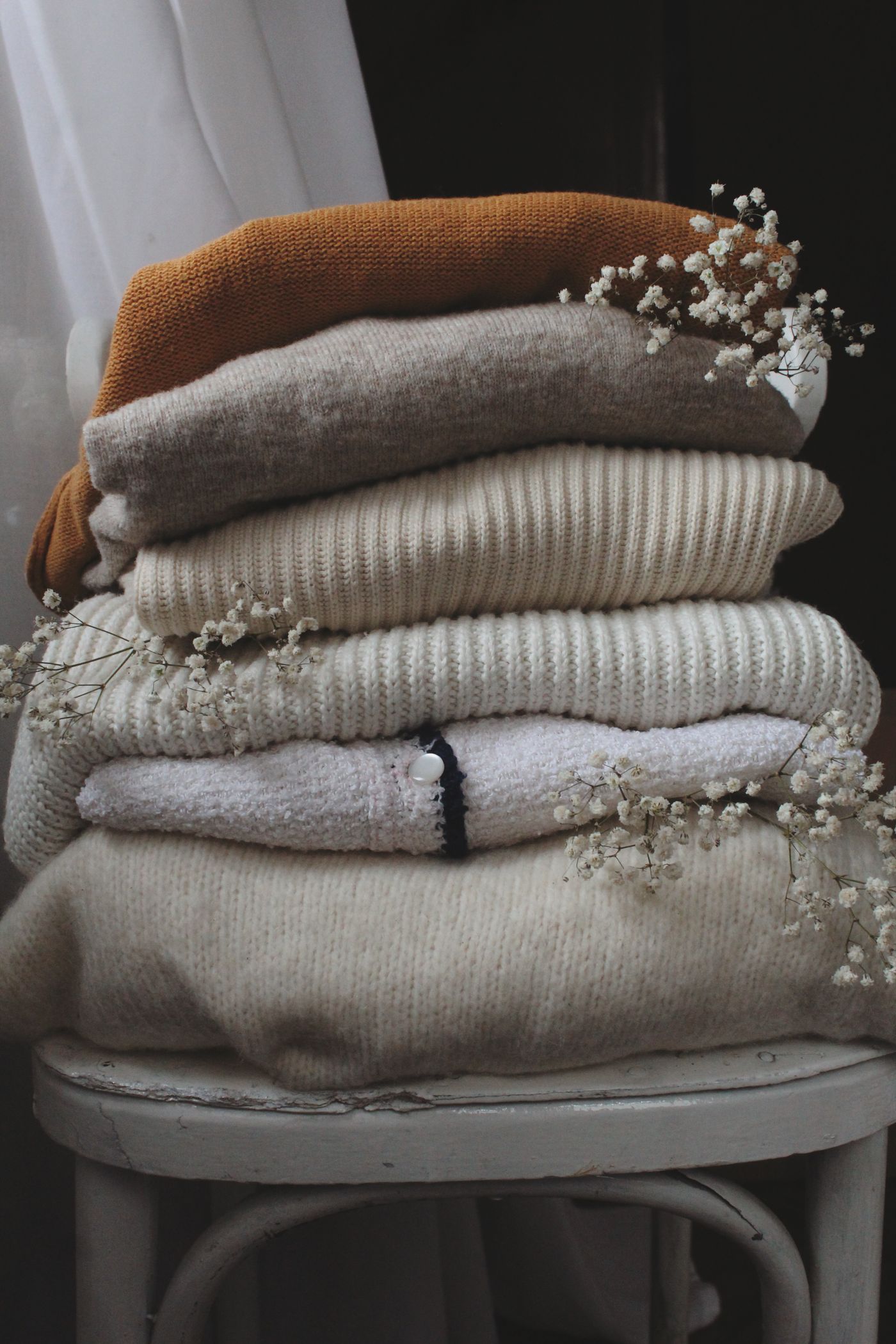 Folded neutral knitwear stacked on a chair.