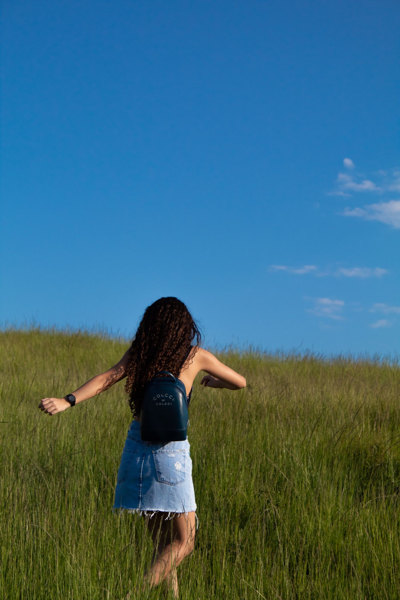 A woman wearing a blue denim skirt while walking across a grassy field.