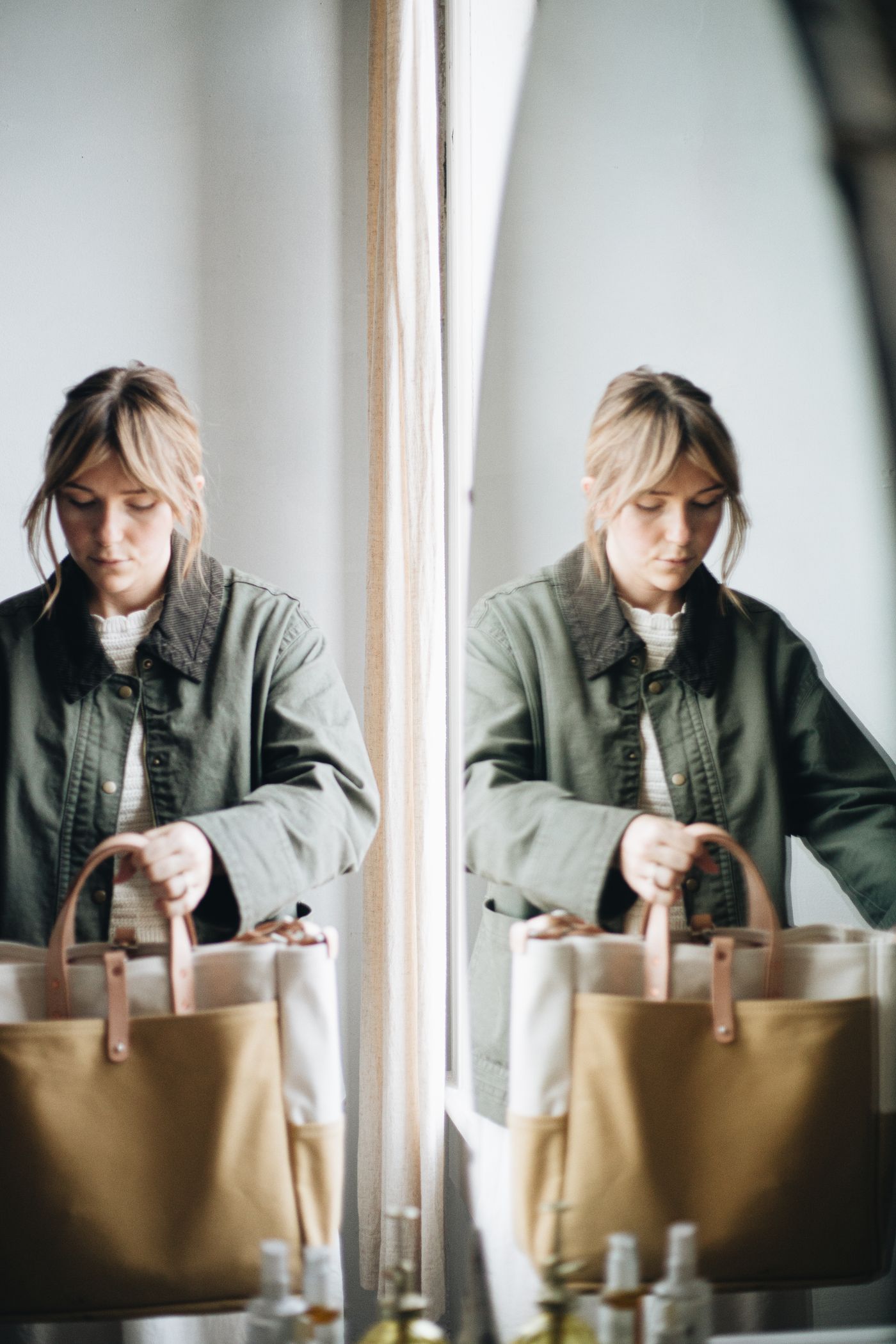 A woman holding a roomy canvas tote beside a mirror.