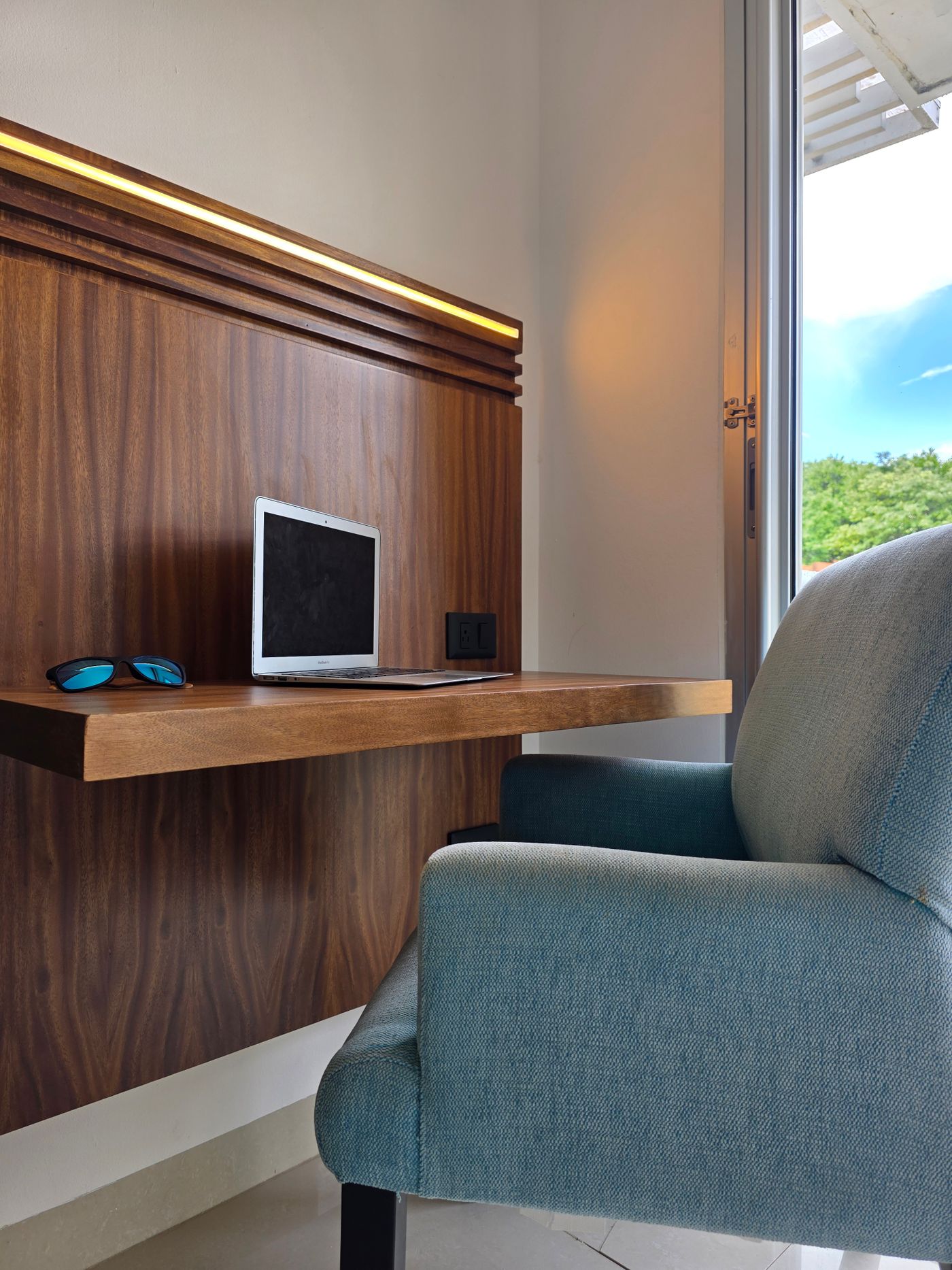 A compact wooden desk and upholstered chair beside a window.