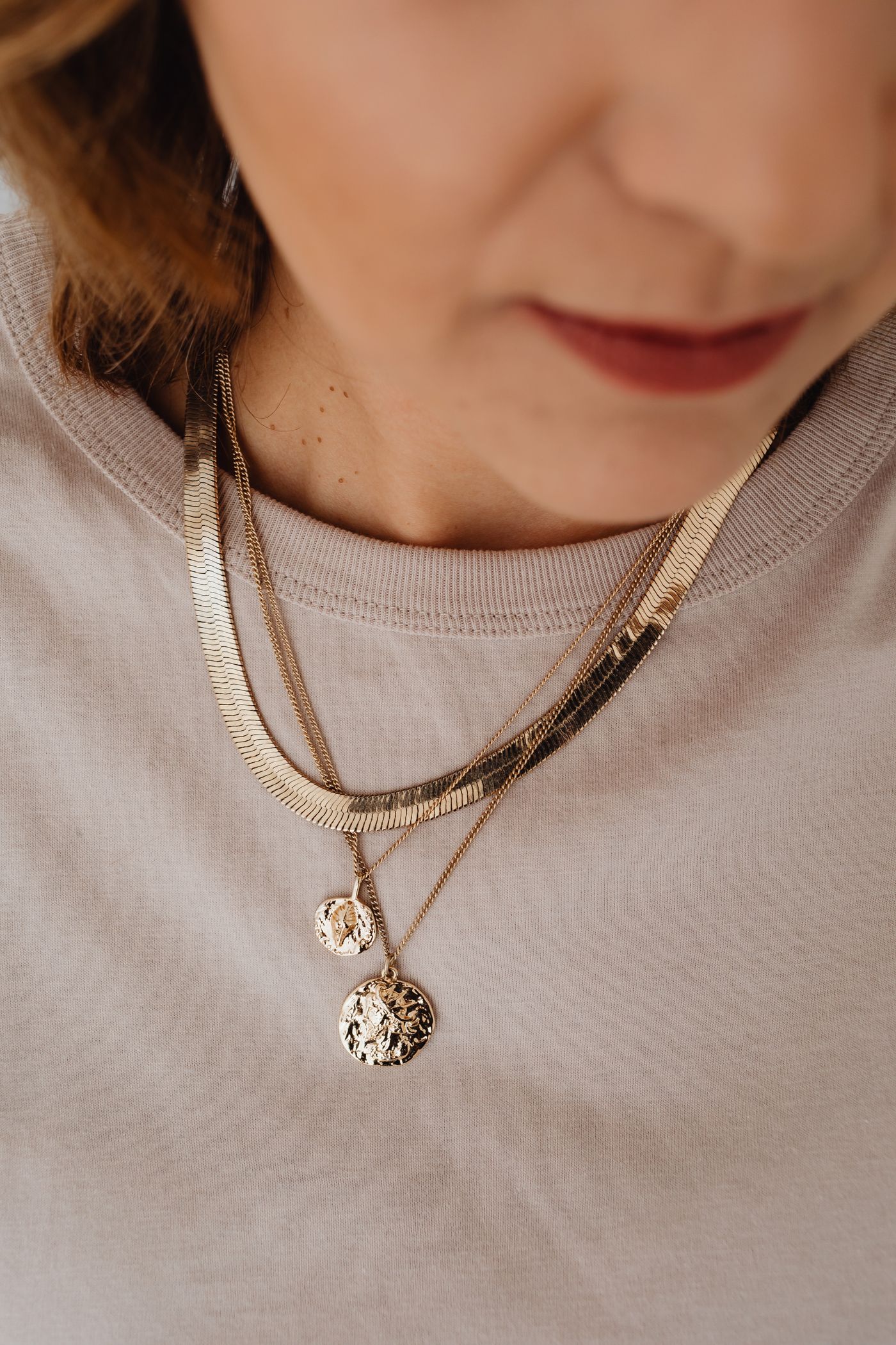 Several necklaces layered over a cream top.