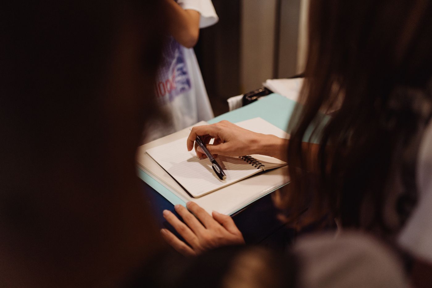 A person writing in a notebook with a pen.