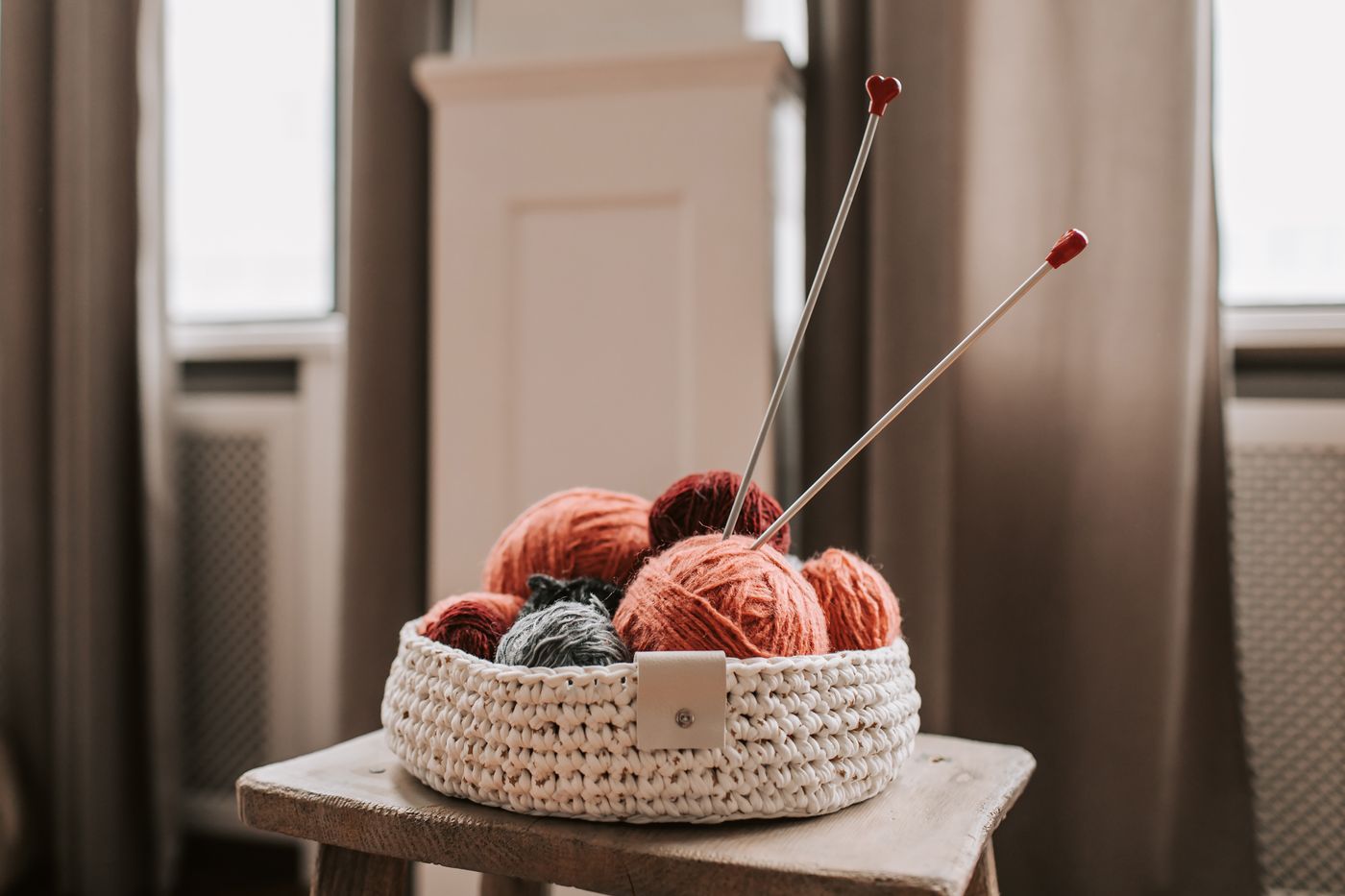 Yarn and knitting needles gathered in a small basket on a stool.