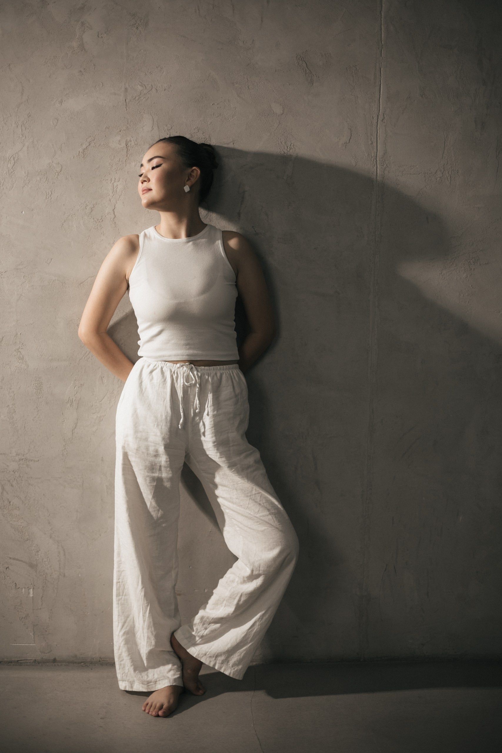 A woman wearing white wide-leg linen trousers with a white sleeveless top.