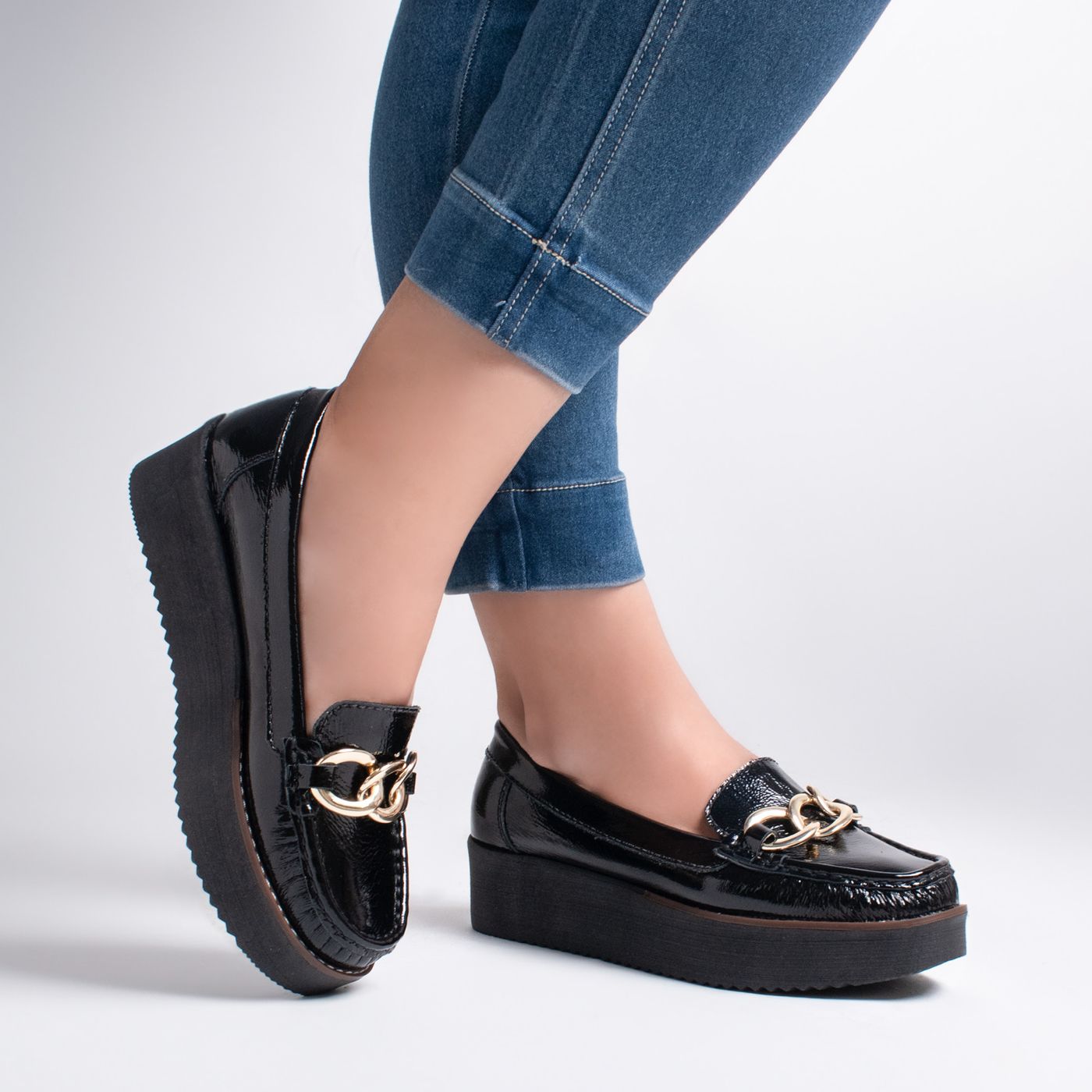 Black loafers with chain details worn with cropped blue jeans.