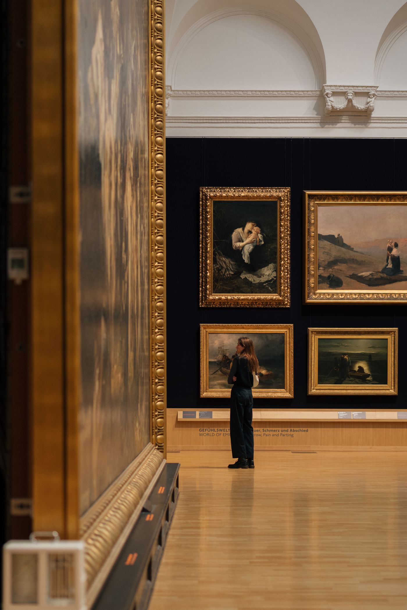 A visitor looking at framed paintings in a museum gallery.