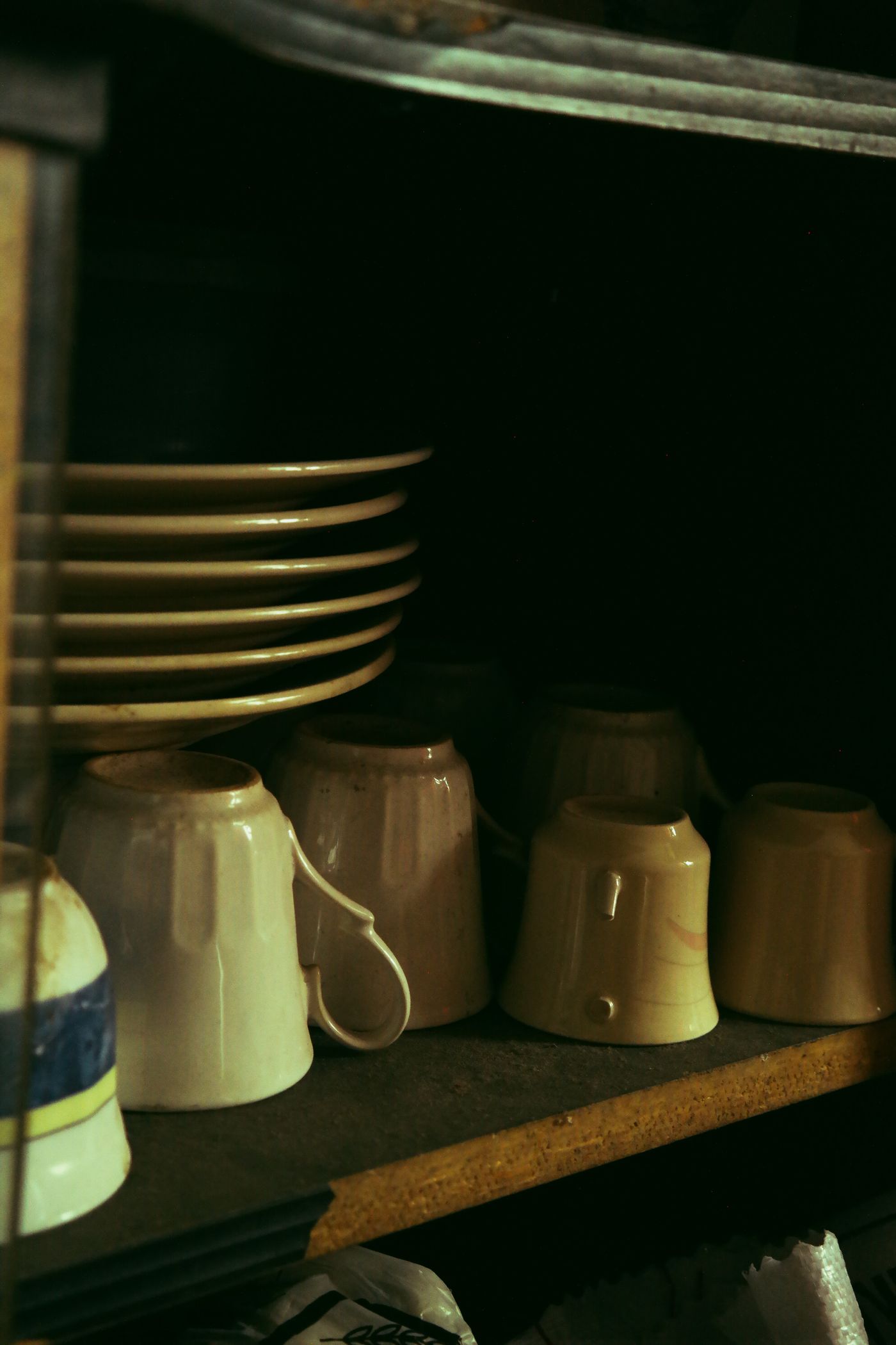 Mugs and stacked plates stored on an open wooden shelf.