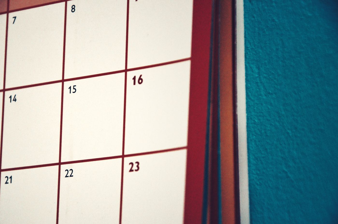 A paper wall calendar hanging against a coloured wall.