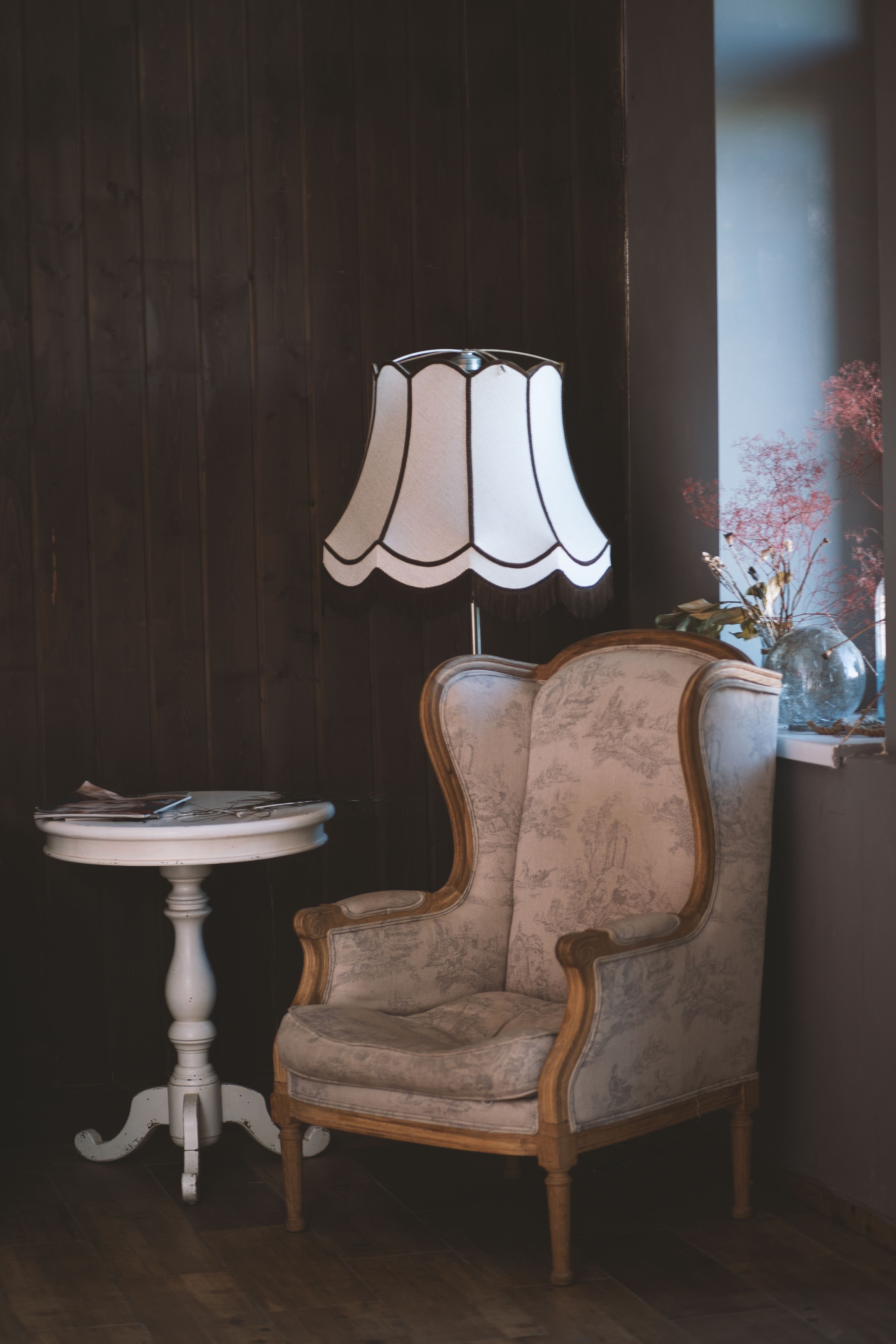 An upholstered reading chair beside a small round table and a shaded floor lamp.