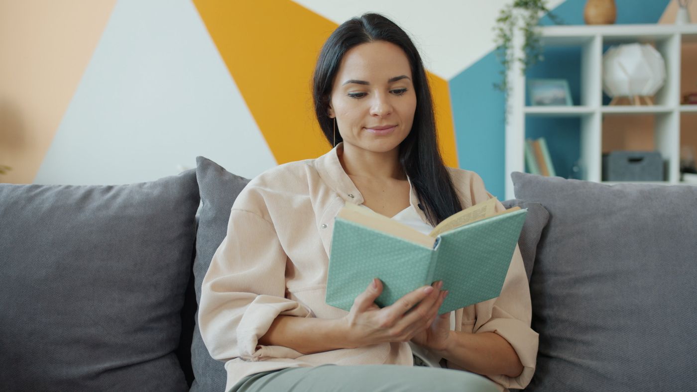 A woman reading a book while sitting on a sofa.