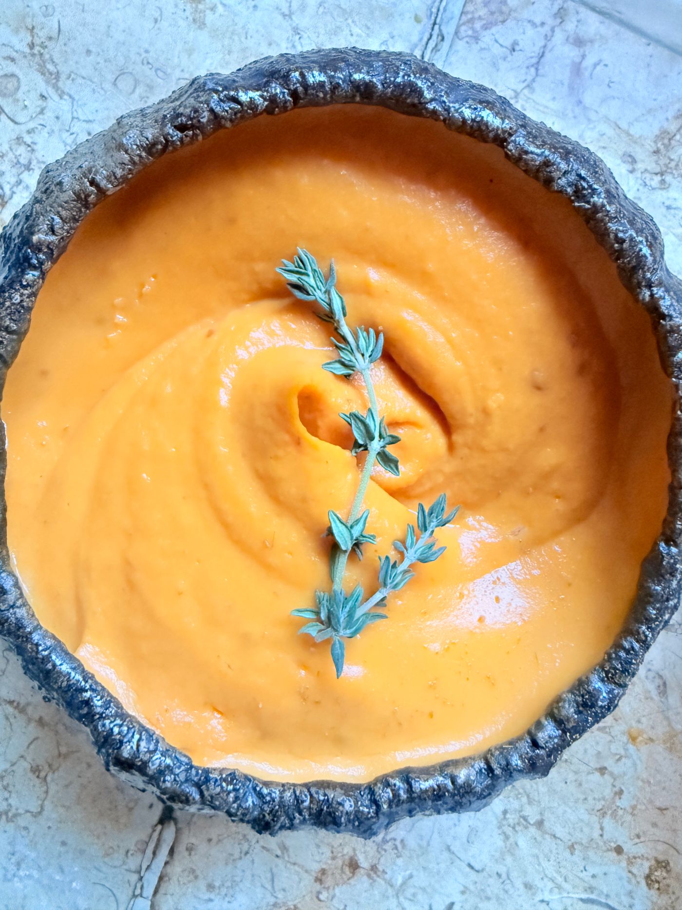 A bowl of smooth orange carrot soup garnished with a sprig of herbs.