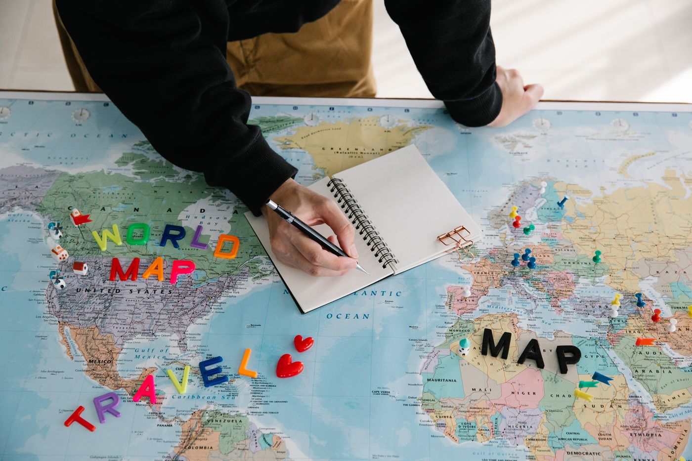 A person writing in a notebook resting on a map.