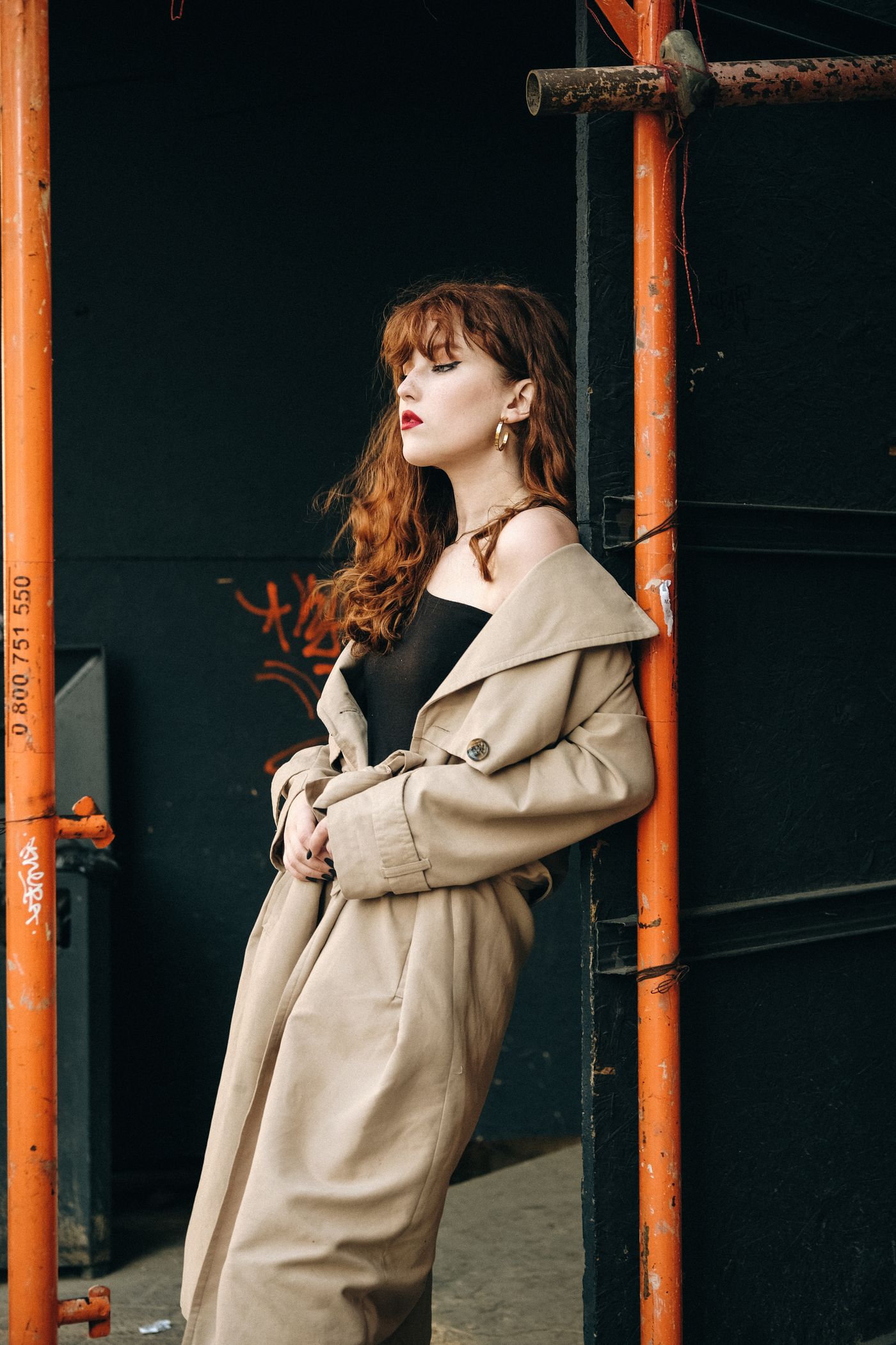A woman wearing a beige belted trench coat over a dark top.
