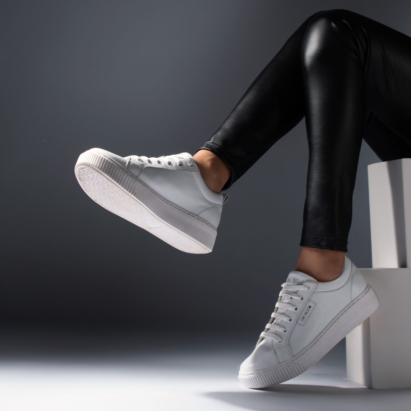White lace-up trainers worn with dark trousers.