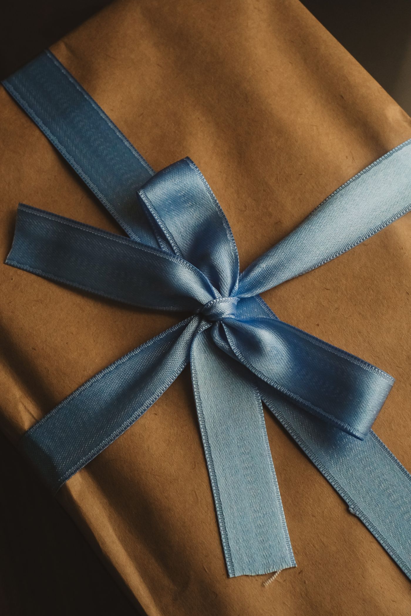 A gift wrapped in brown paper and tied with a blue satin ribbon.